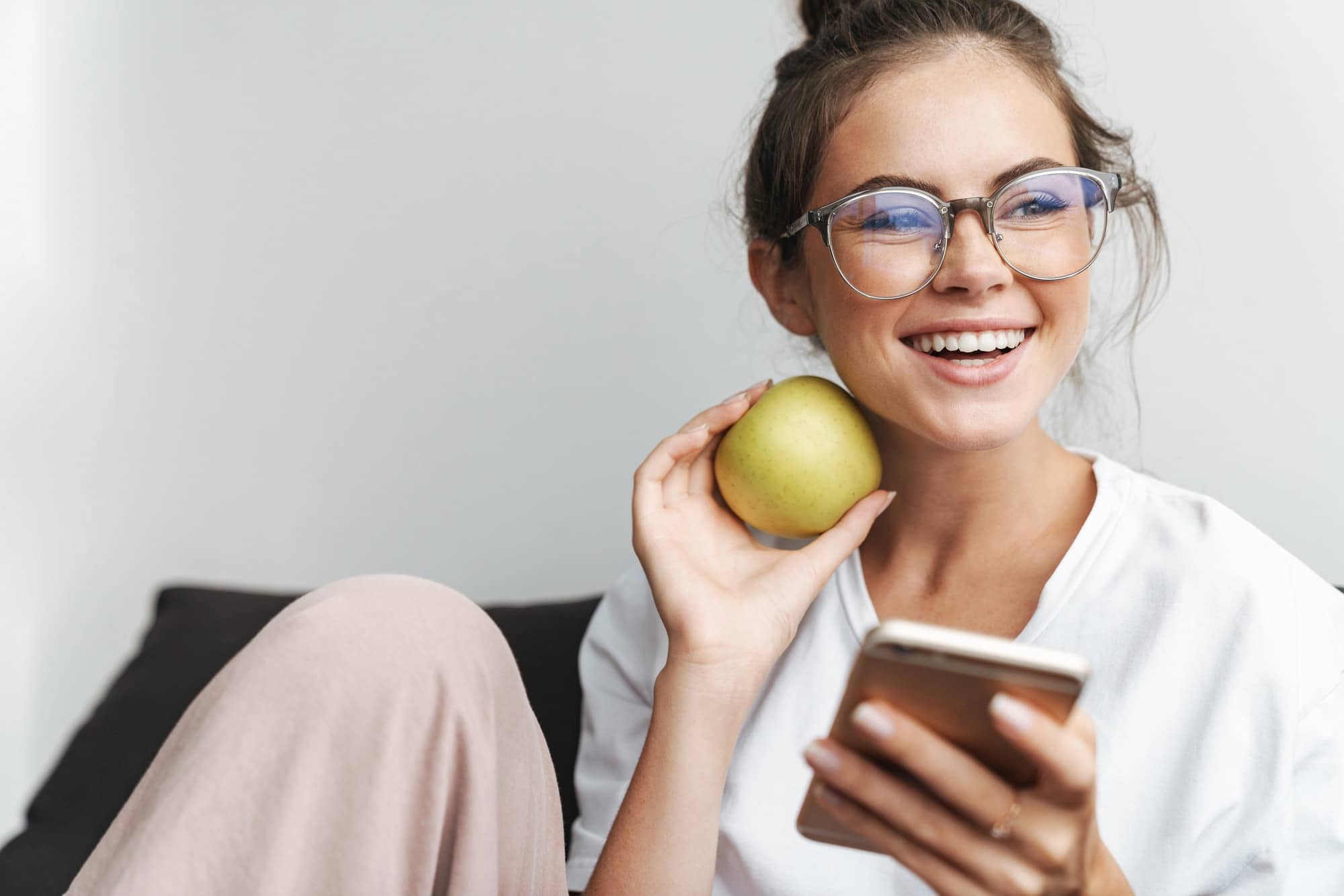 Image of smiling nice woman using cellphone and holding apple