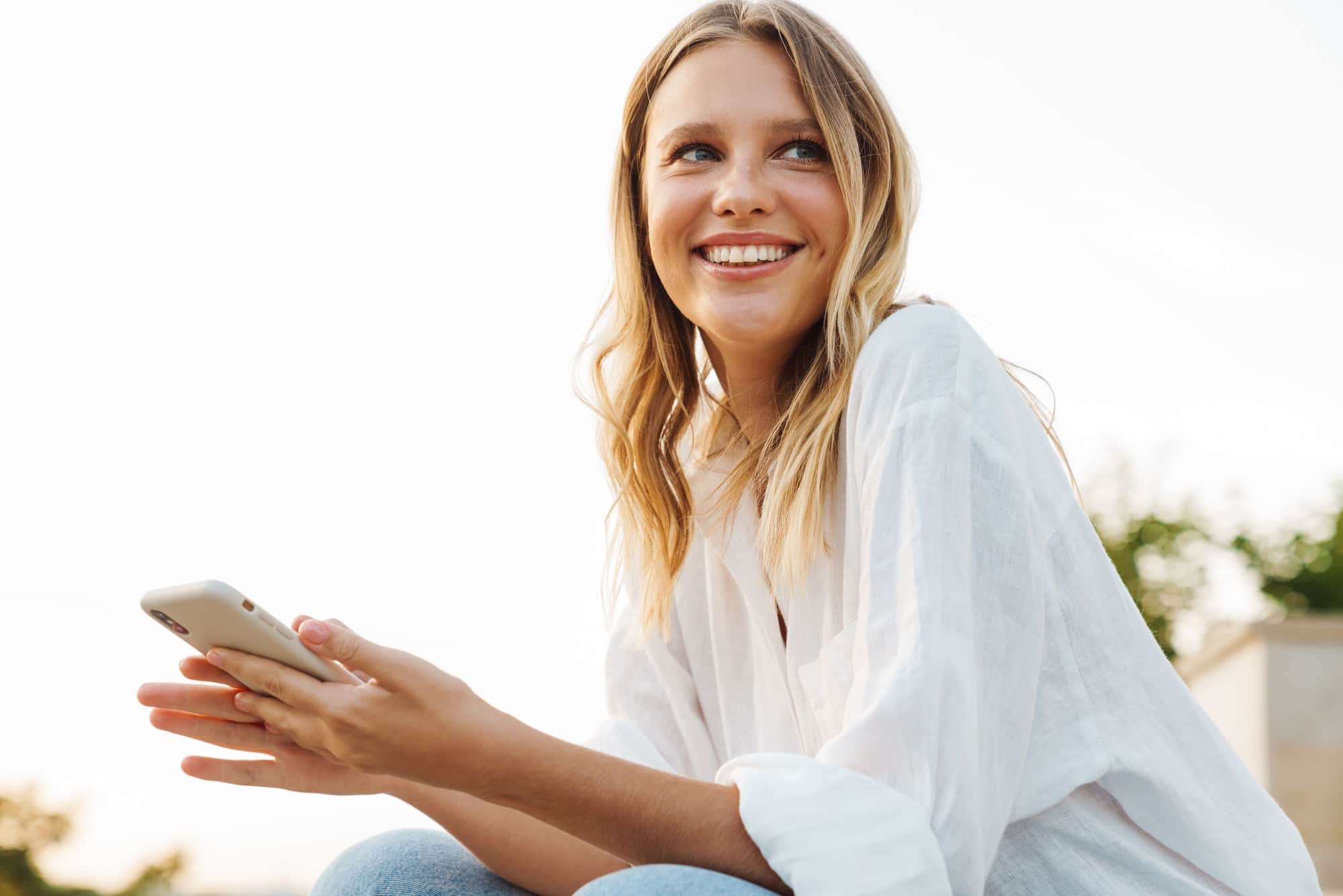 Nice happy woman smiling and using mobile phone while sitting outdoors