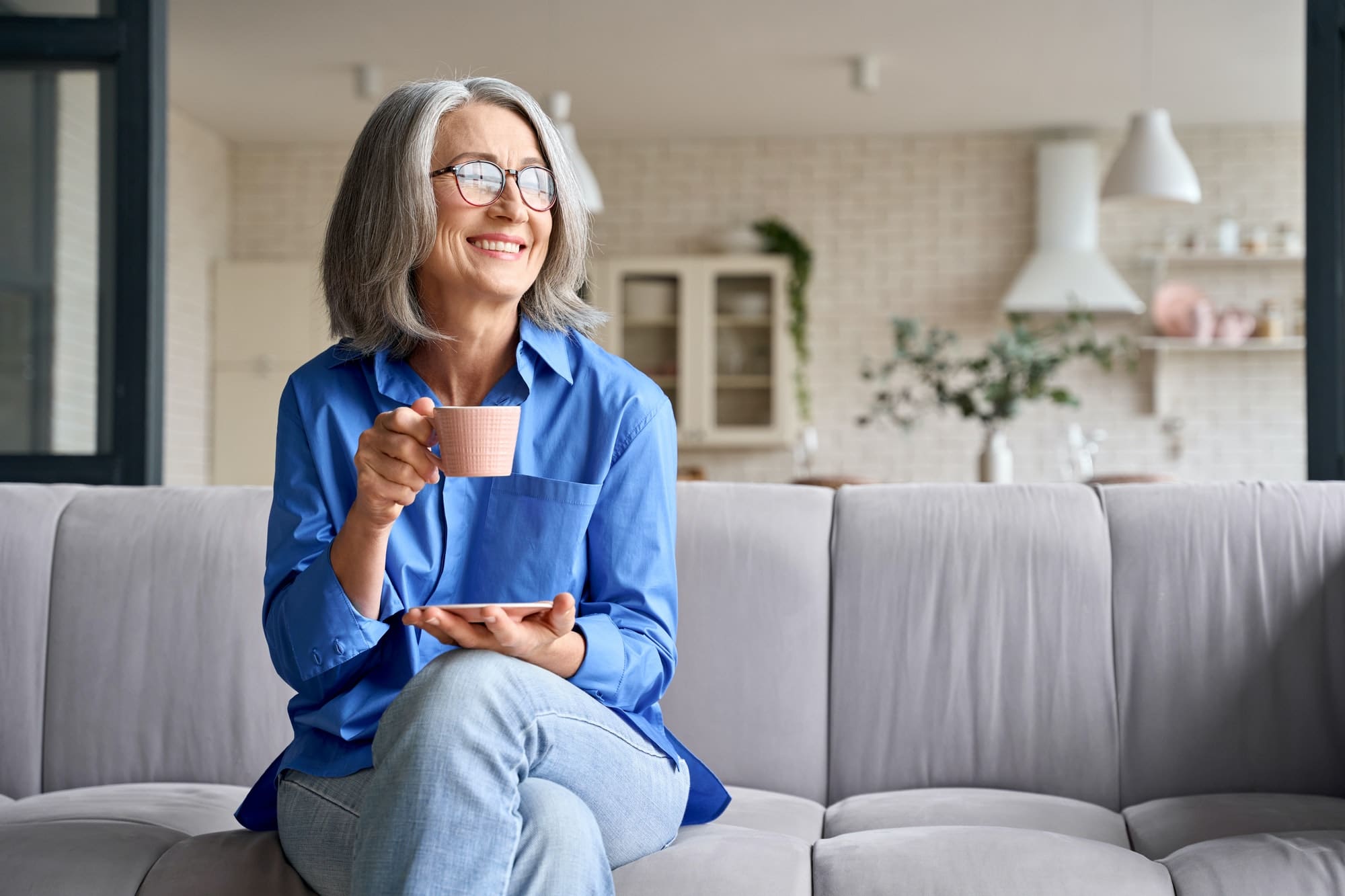 Senior smiling 60s woman portrait at home looking away with cup of tea, coffee.